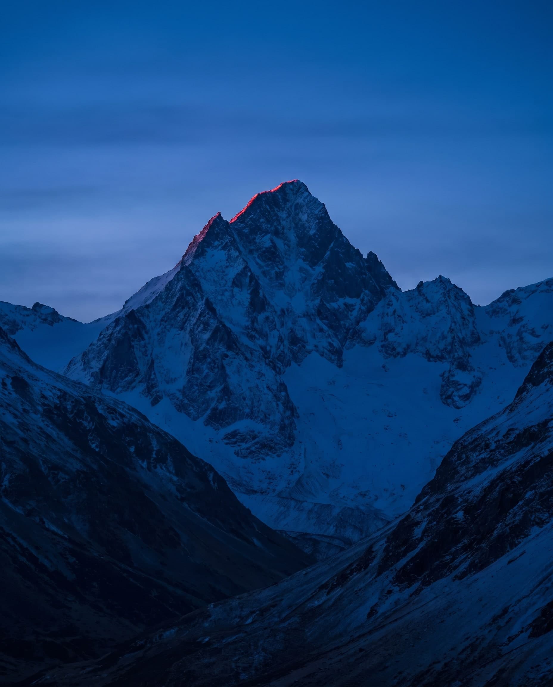 Verschneiter Berggipfel in der blauen Stunde, der oberste Grat im ersten Licht