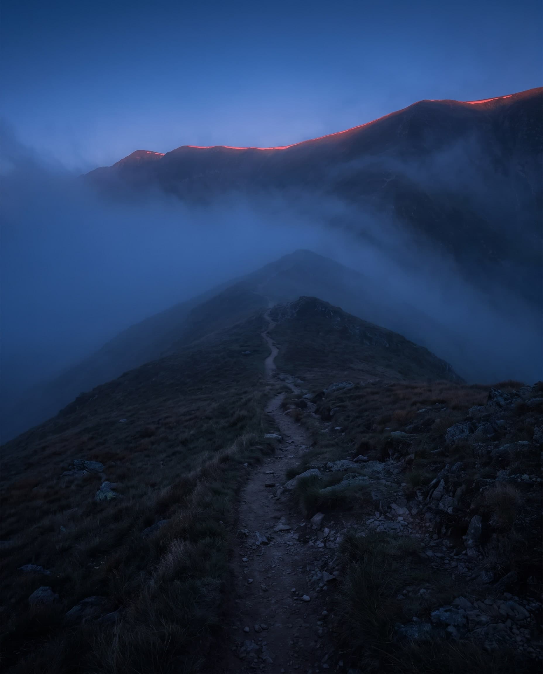 Schmaler Pfad über einen Berggrat im Nebel, der Grat fängt das erste Licht