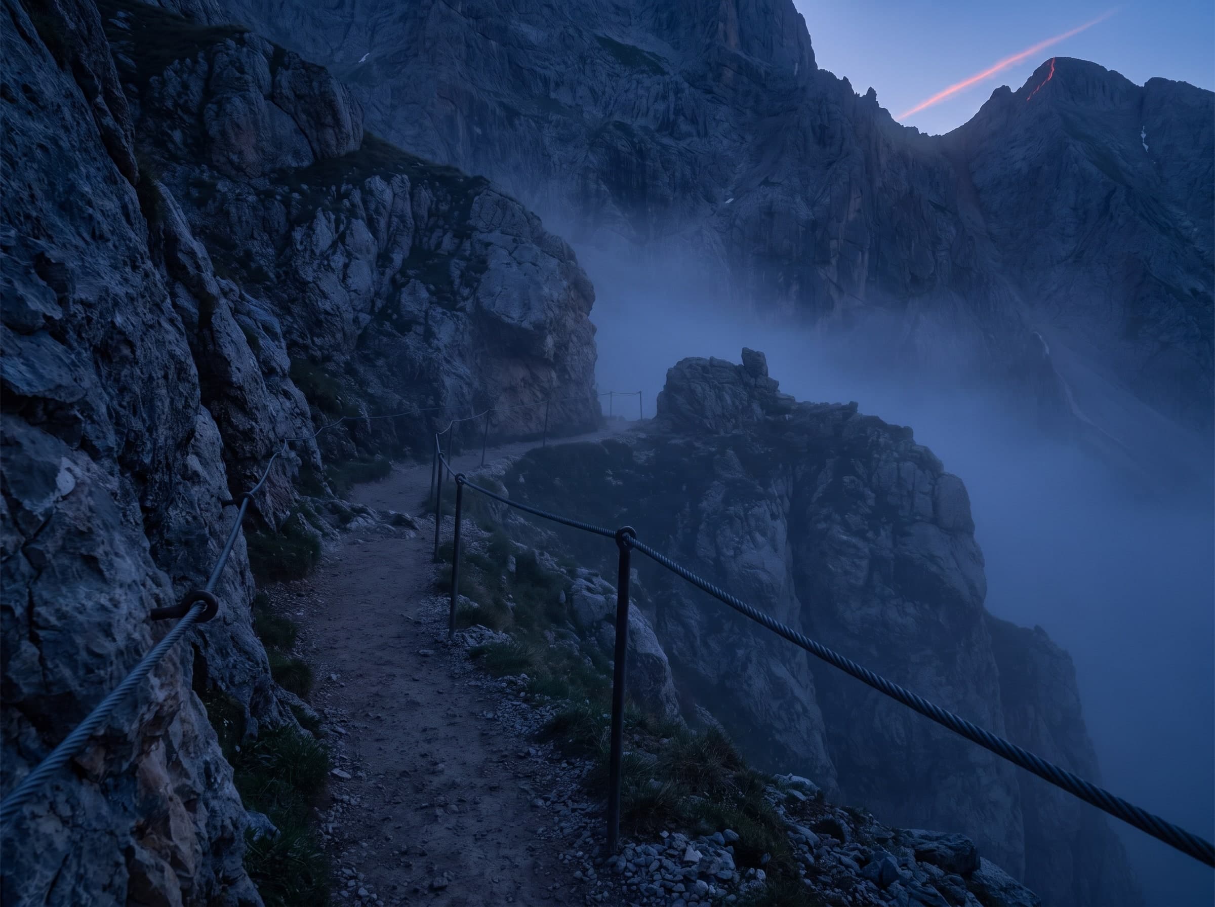 Bergpfad entlang einer Felswand, gesichert mit einem Stahlseil als Handlauf, Nebel in der Schlucht